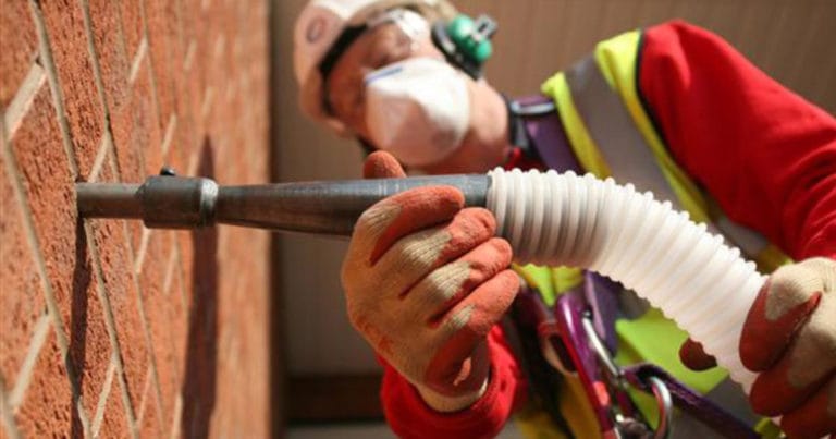 Vakman brengt spouwmuurisolatie aan in de buitenmuur van een woning