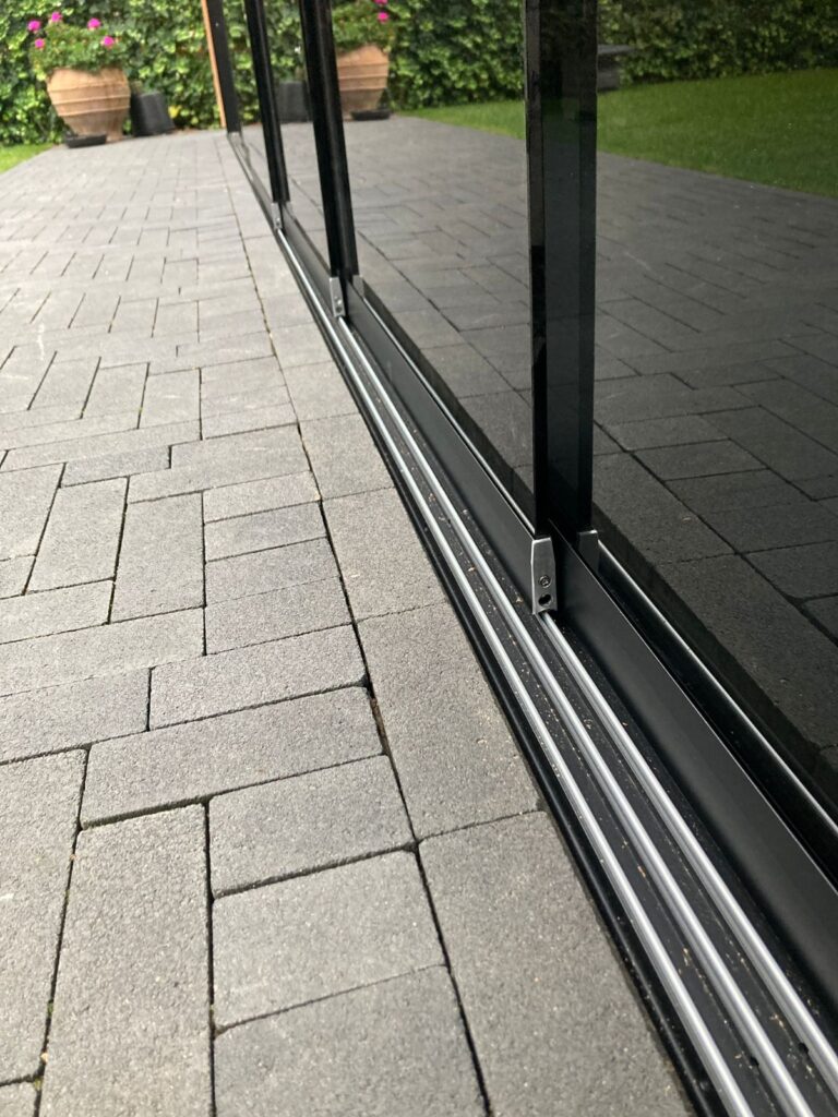 Detail van railsysteem met zwarte glazen schuifpanelen bij overkapping in Delft