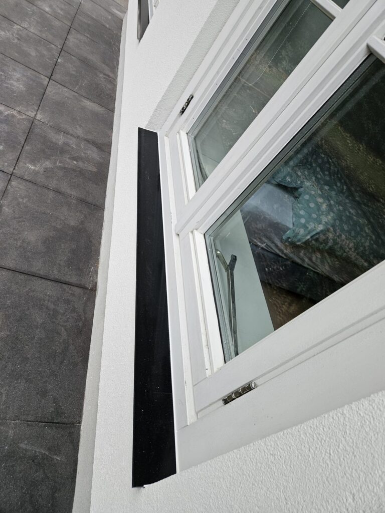 Detail van zwart afgewerkte raamdorpel onder wit houten raamkozijn