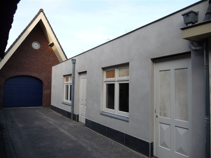 Gerenoveerde zijgevel in Gouda met licht gevelpleisterwerk, witte kozijnen en donkere plint